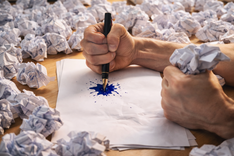 Haut d'une pile de papier froissé et raturé sur un bureau, symbolisant la frustration de rédiger un courrier de litige administratif.